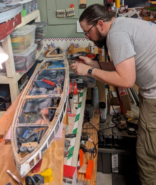 a man uses a Dremel tool to work on an unfinished model